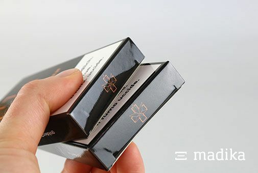 Kleine Faltschachteln, bedruckt und veredelt Zwei glänzend veredelte kleine Faltschachteln werden hochgehalten, um den bedruckten Boden zu zeigen.