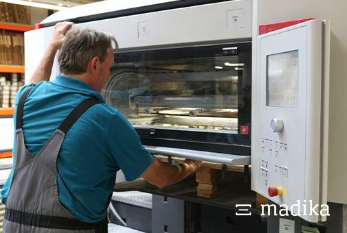 Blick in die Offsetmaschine: Der Drucker entnimmt einen Papierbogen und überprüft den Druck. Offsetdruck einer bedruckten Faltschachtel